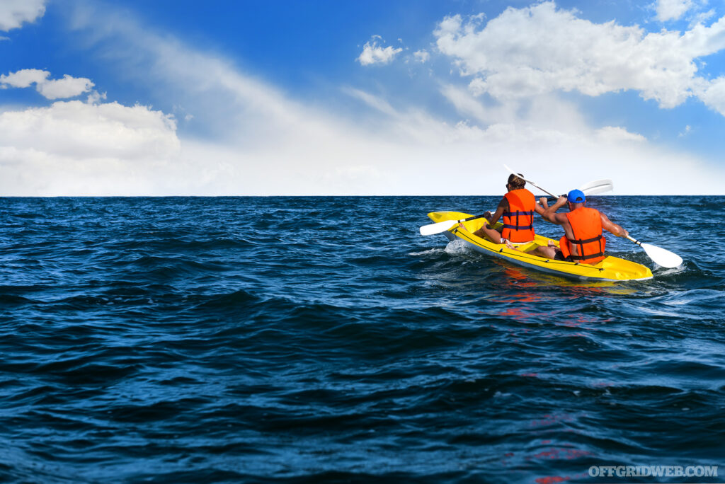 Two people kayaking on open water. They are both wearing personal flotation devices to demonstrate their importance in regard to cold water safety.