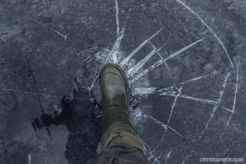 A view of a foot as seen from above, stepping on to ice. The ice is beginning to crack beneath the weight. 