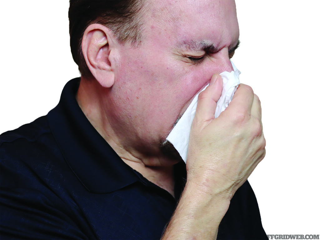 Photo of an adult male sneezing into a tissue.