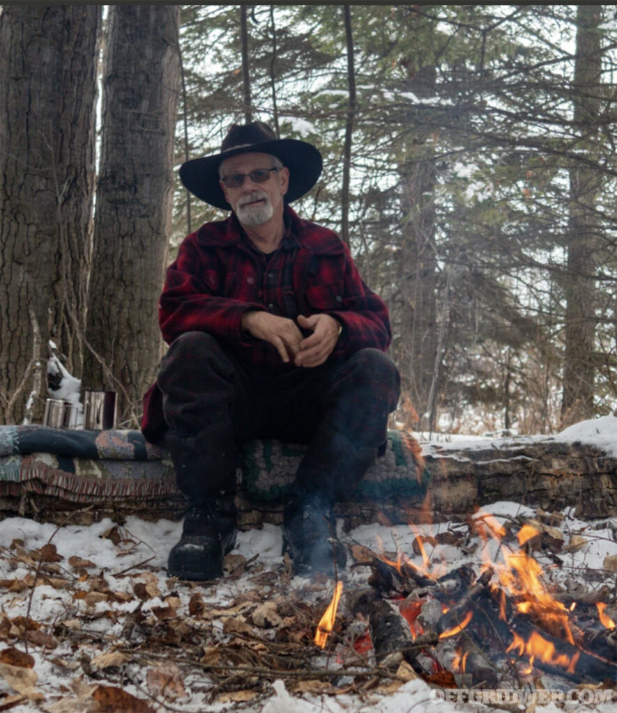 Photo of Ross Hinter sitting by camp fire in winter.