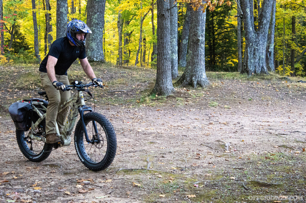 Photo of an adult male riding an eBike on a forested, unpaved trail.