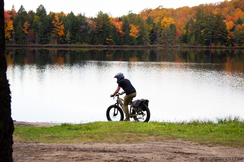 Photo of an adult riding an eBike next to a lake in autumn with the leaves changing color in the background.