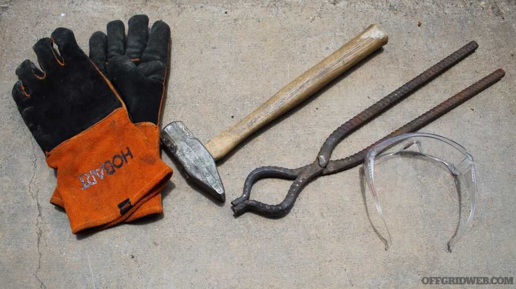 Photo of essential blacksmithing tools. From left to right: leather gloves, hammer, tongs and safety glasses.