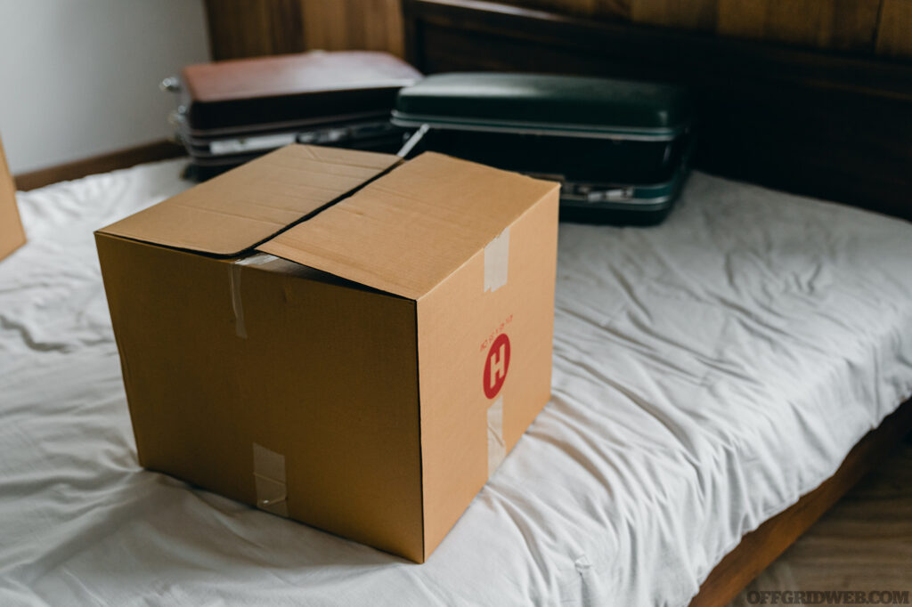 Photo of a moving box and several suitcases lying on an unmade bed in preparation for a move.
