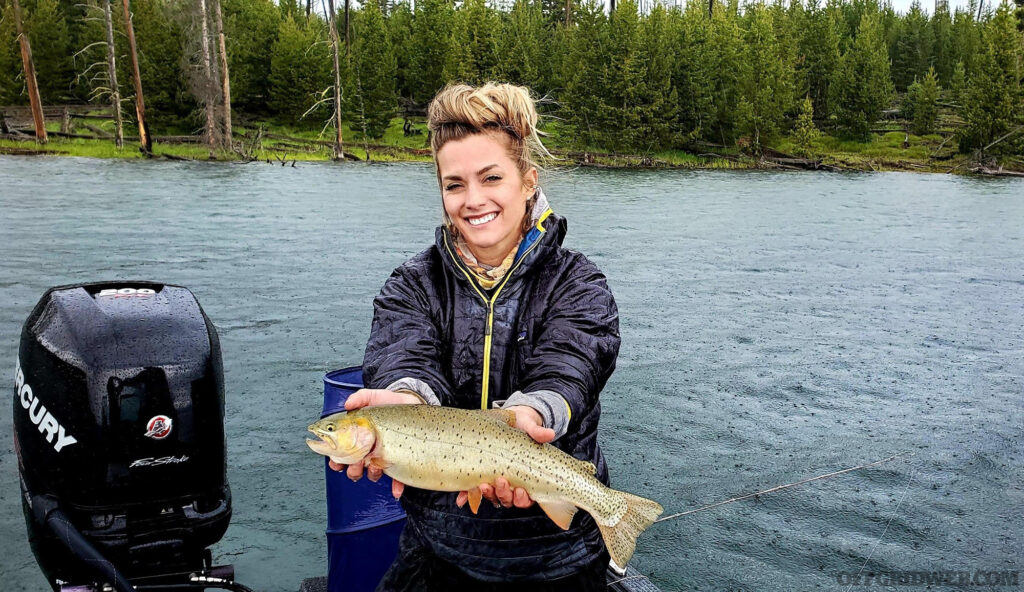 Photo of Melissa Miller fishing from a boat on a lake, holding up a fish she caught.