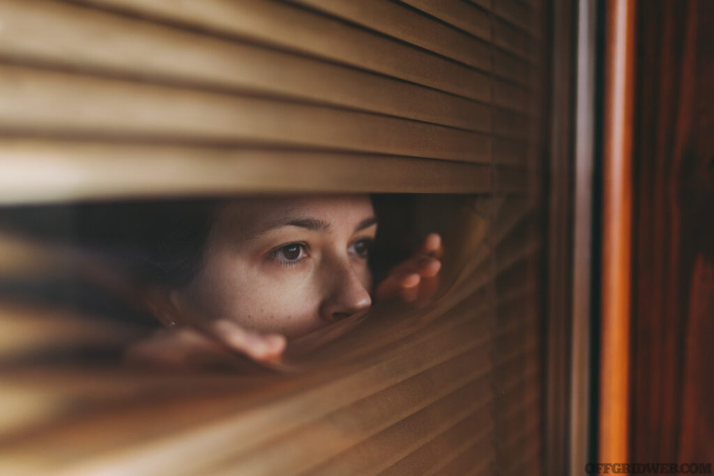 Photo of a woman peering through closed blinds, during a modern day witch hunt.