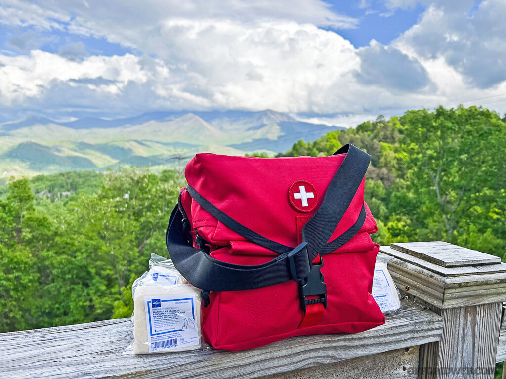 Photo of a red first aid kit on the railing of a wooden balcony with a panoramic view of a forest in the background.