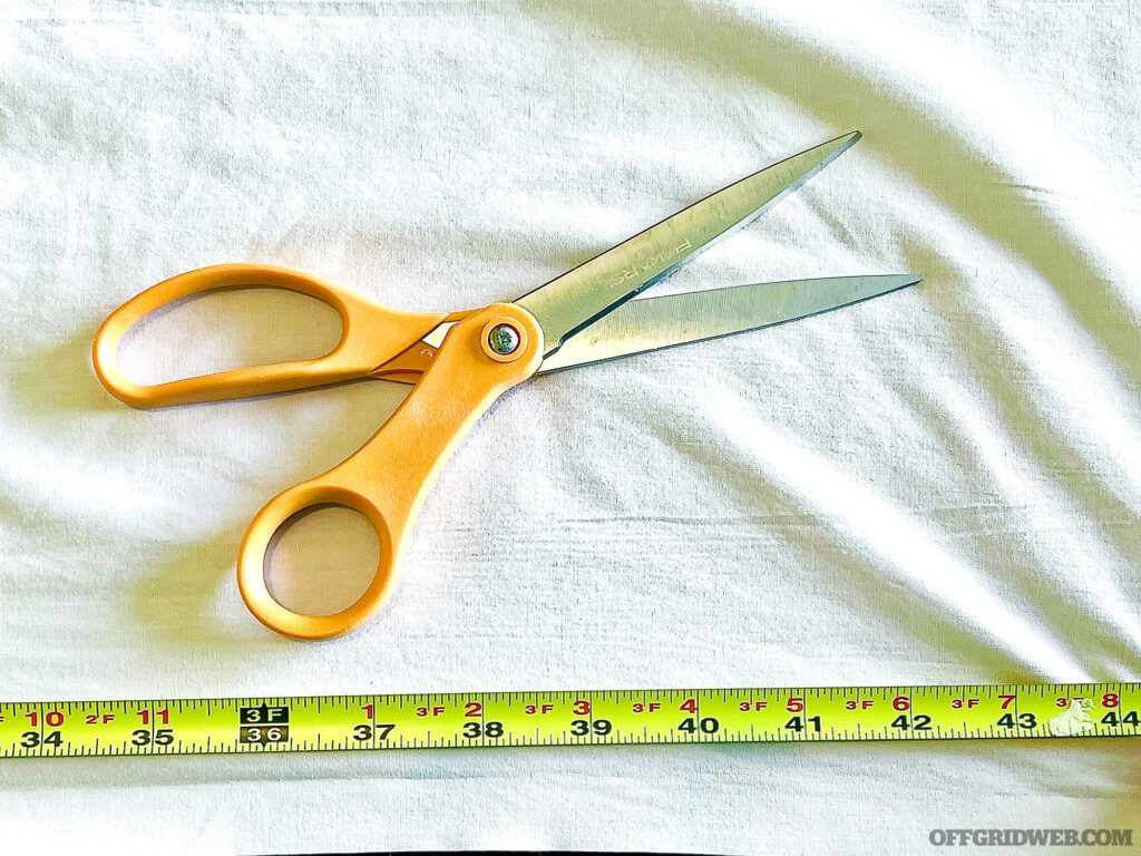 A scissors, measuring tape and white cloth used to make a triangular bandage.