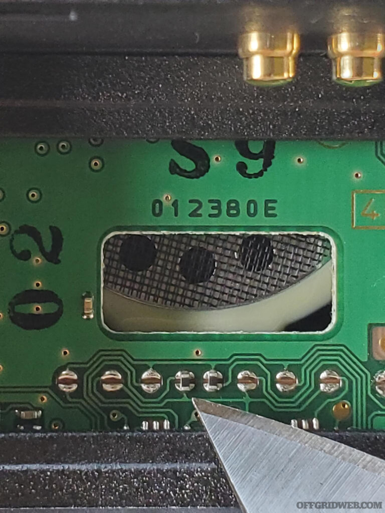 Identify the soldered jumpers (4th and 5th from the left) underneath the cutout on the PCB.