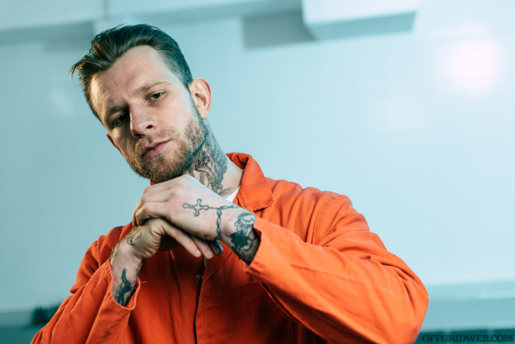 Prisoner with tattoos looking at camera in prison cell.