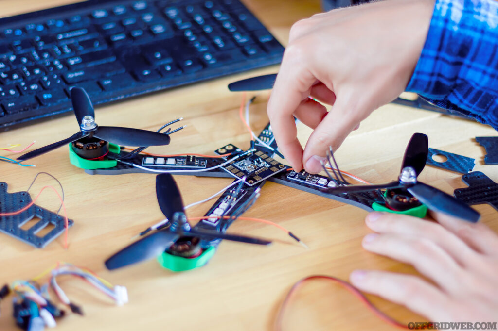 Closeup programmer hands are making electronic FPV drone at home office. Man developer is building constructing DIY quadcopter from kit with microcontrollers at workplace. Desktop of hardware engineer