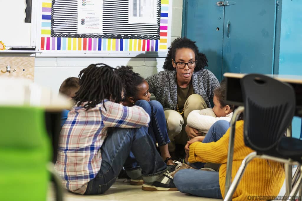 A group of seven school children and their teacher doing a practice drill, sheltering in place, sitting on the floor in a corner of their classroom.